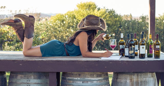 Girl in cowgirl hat and boots lays on her belly pouring wine with many California wines to choose from